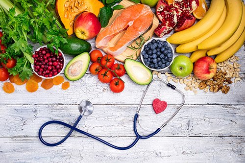 A stethoscope with a heart sits next to various fruits and vegetables