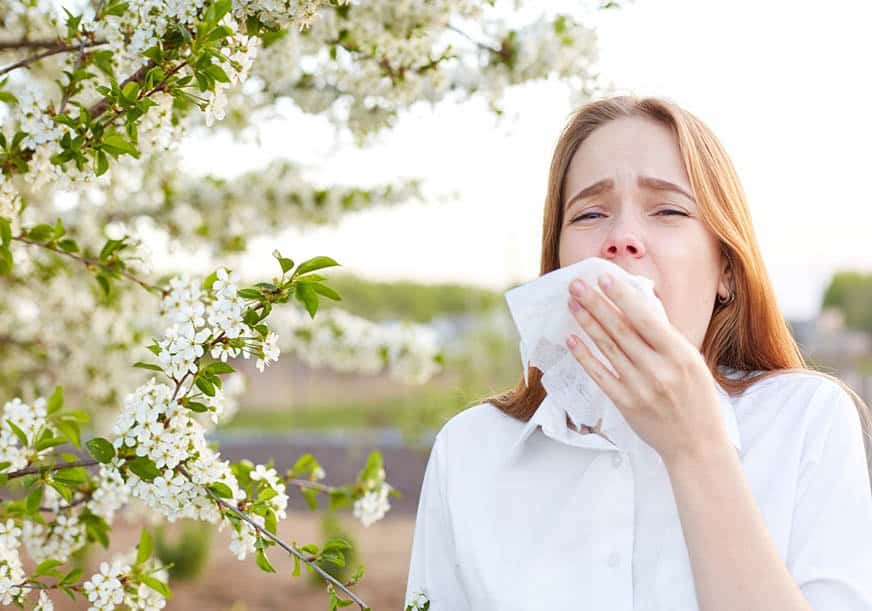a woman sneezes in front of a tree