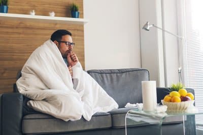 A man wrapped in a blanket coughs on a couch