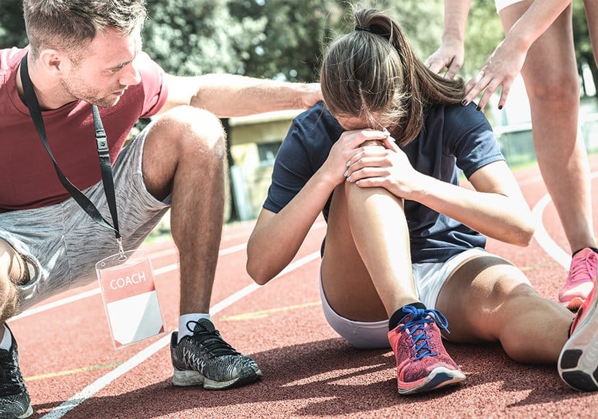 A runner has fallen and clutches her knee in pain