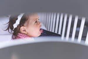A baby holds her mouth open in a crib