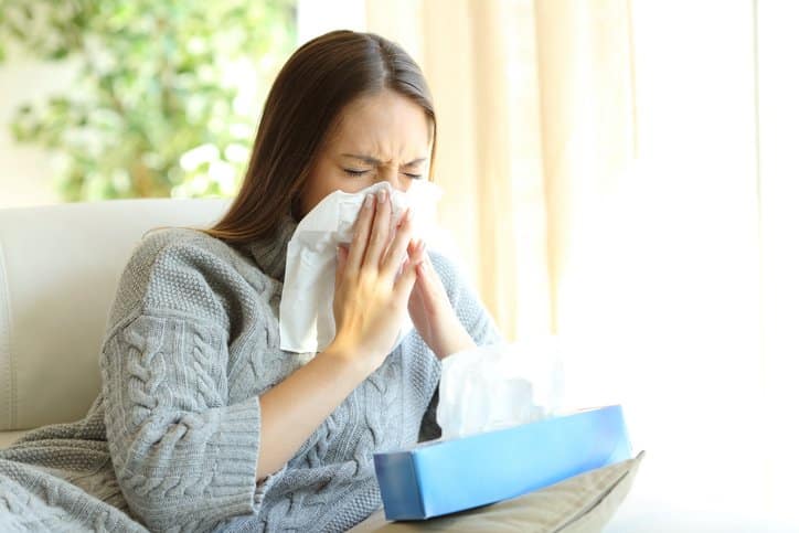 A woman sneezes on her couch