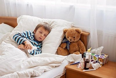 A sick child lays in bed with his teddy bear
