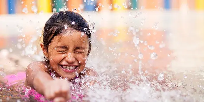 Little girl swimming in a pool with water splashing around her, eyes closed.