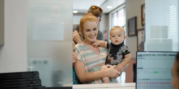 Smiling mother holding her baby while checking in at an urgent care front desk.